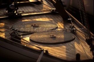 Coiled ropes and mooring lines on the foredeck of a classic yacht moored in the golden sunset