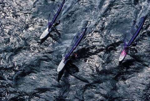 Three European Champion Mistral windsurfers sailing across a textured sea in formation