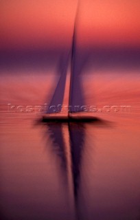 Reflection of model yacht on still water at sunset