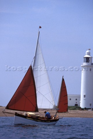 Traditional Cornish Crabber sailing by lighthouse