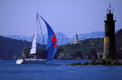 Cruising yacht sailing past a lighthouse into a sheltered bay 