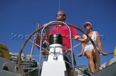 Woman sitting behind man helming cruising yacht 