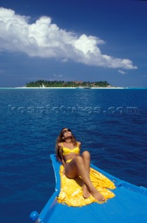 Beautiful female girl model lying on a towel in a stylish yellow bikini onboard a turquoise blue traditional fishing boat, sunbathing by a tropical island sandy beach