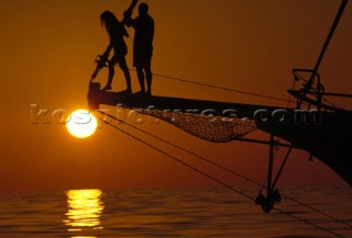 Romantic sunset as a couple stand on a classic yacht bow sprit in the Malvies, Indian Ocean
