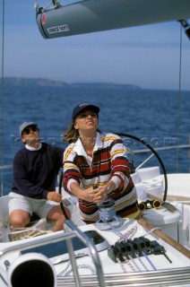 Woman tailing wich and man behind wheel of cruising yacht