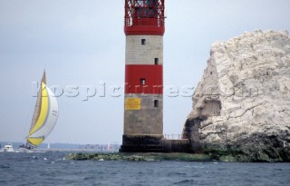 A sailing yacht under spinnaker runs aground on Goose Rock by the Needles lighthouse, Isle of Wight, UK