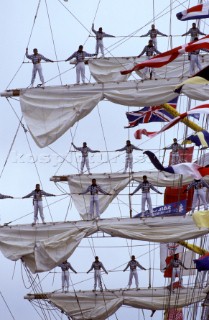 Tall ship crew standing on footlines of yard arm in cerimonial tradition