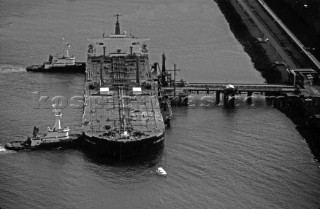 Fully laden oil tanker is pushed onto the dock by two tug boats