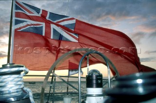 Red British ensign flying in the wind off stern of sailing yacht