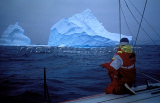 A sailor admires two huge icebergs from the deck of a racing yacht