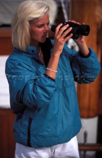 Woman looking through binoculars on board classic yacht  Man on boat using hand-held GPS instrument  Woman looking through binoculars on board classic yacht