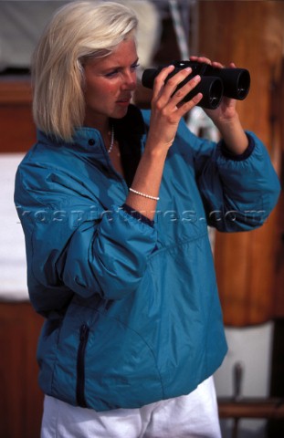 Woman looking through binoculars on board classic yacht  Man on boat using handheld GPS instrument  