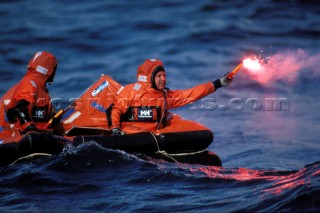 Two crew in red survival suits in a life raft holding flare awaiting rescue