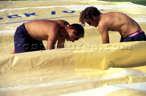 Two crew members from Dolphin repair a broken sail 