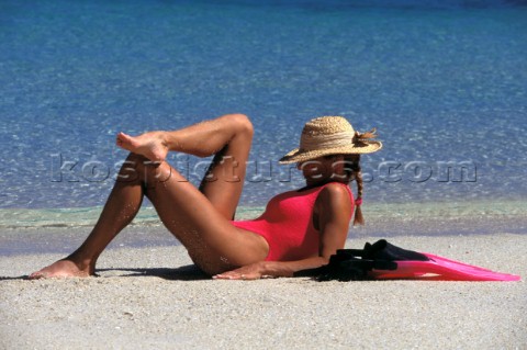 Model girl Jilly Johnson with straw hat lying on a sandy beach in Australia with pink swimsuit and f