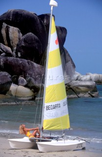 Model on beaced sailing dinghy with the sail up