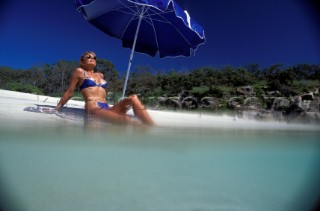 Girl taking shade under blue umbrella at waters edge