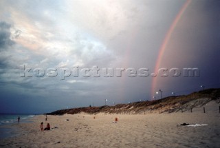 A rainbow over a cloudy sky above a sandy beach