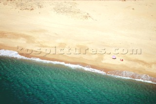 Aerial view of a couple sitting on a deserted beach by the shade of an umbrella