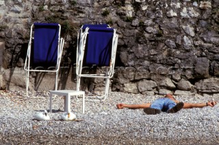 Man lying on beach next to two deckchairs