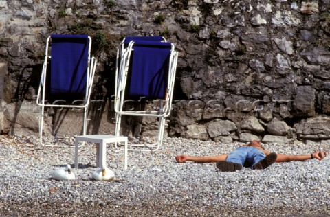 Man lying on beach next to two deckchairs 