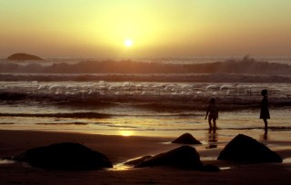 Two children standing in surf on beach at sunset