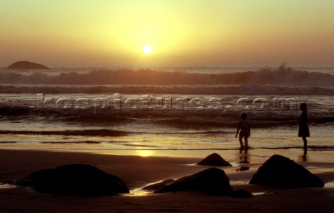 Two children standing in surf on beach at sunset 