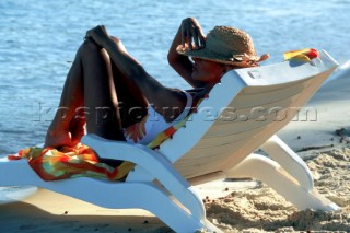 Woman in straw hat sunbathing on a white sun lounger close to the water on a sandy beach