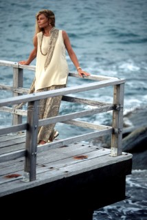 Woman leaning on rail of wooden veranda overlooking the sea