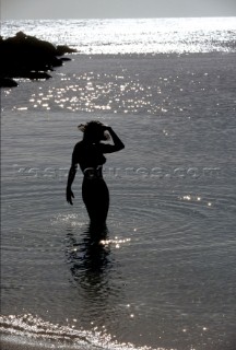 Silhouette of naked woman with hand on head standing in shallow water