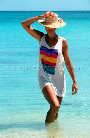 Woman in straw hat and long vest walks out of the sea
