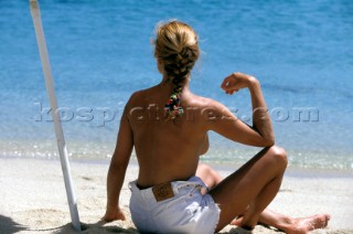Topless woman in white shorts on sandy beach looking out to sea