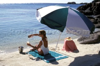 Woman pours a glass of champagne under the shade of a beach umbrella