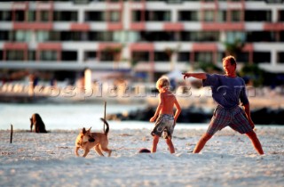 A father and son play with their dog on a sandy beach