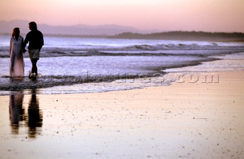 A couple take a romantic walk along a deserted beach at sunset