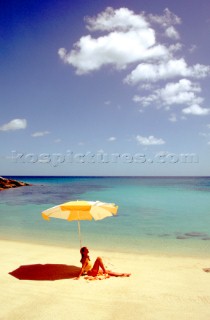 A woman sits alone on a deserted beach under a yellow umbrella