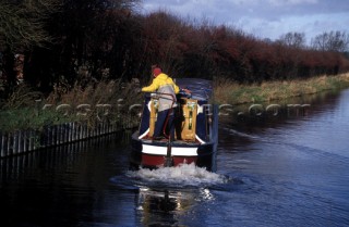 Man at the helm steers a narrow boat to the bank on the Kennet and Avon canal.