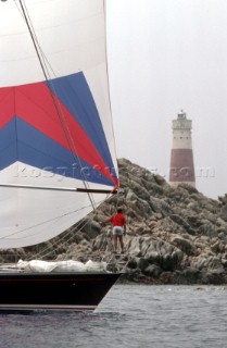 Bowman on foredeck of sailing yacht with lighthouse and rocks in background, Sardinia