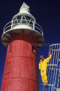 Man in yellow sailing gear standing next to a red lighthouse
