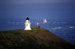 Lighthouse on top of cliff overlooking cruising yacht at sea