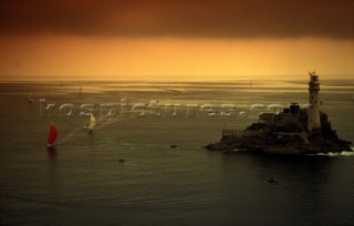 Two racing yachts approach the Fastnet rock at dawn