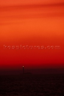 Lighthouse on rocks under red sky