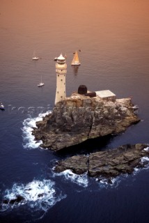 A single yacht sails round the Fastnet rock at dawn
