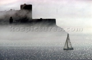 Yacht sailing in fog on calm sea with lighthouse in background