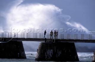 People watch a huge crashing wave from a pier