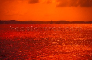 Yachts sailing in the distance under a red sky, Solent, UK