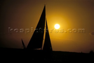 Sun behind silhouette of sails in moody sky