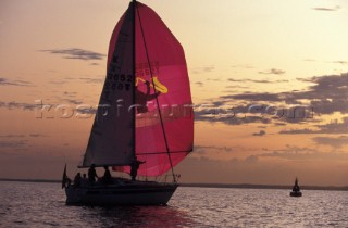 Crusing yacht under red spinnaker at sunset