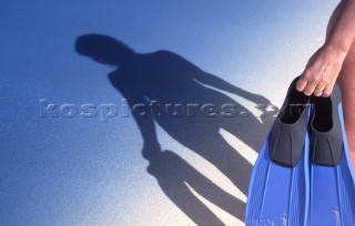 Silhouette of diver carrying flippers and fins on a sandy beach