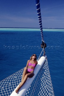Woman lying on bowsprit of sailing yacht.